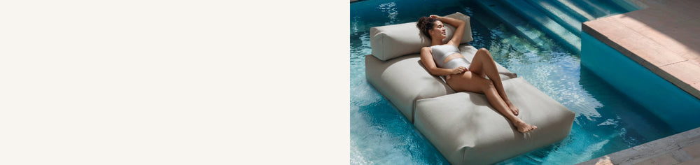Eine Frau liegt entspannt auf einem Poolsofa double in Beige, das im Pool schwimmt. 