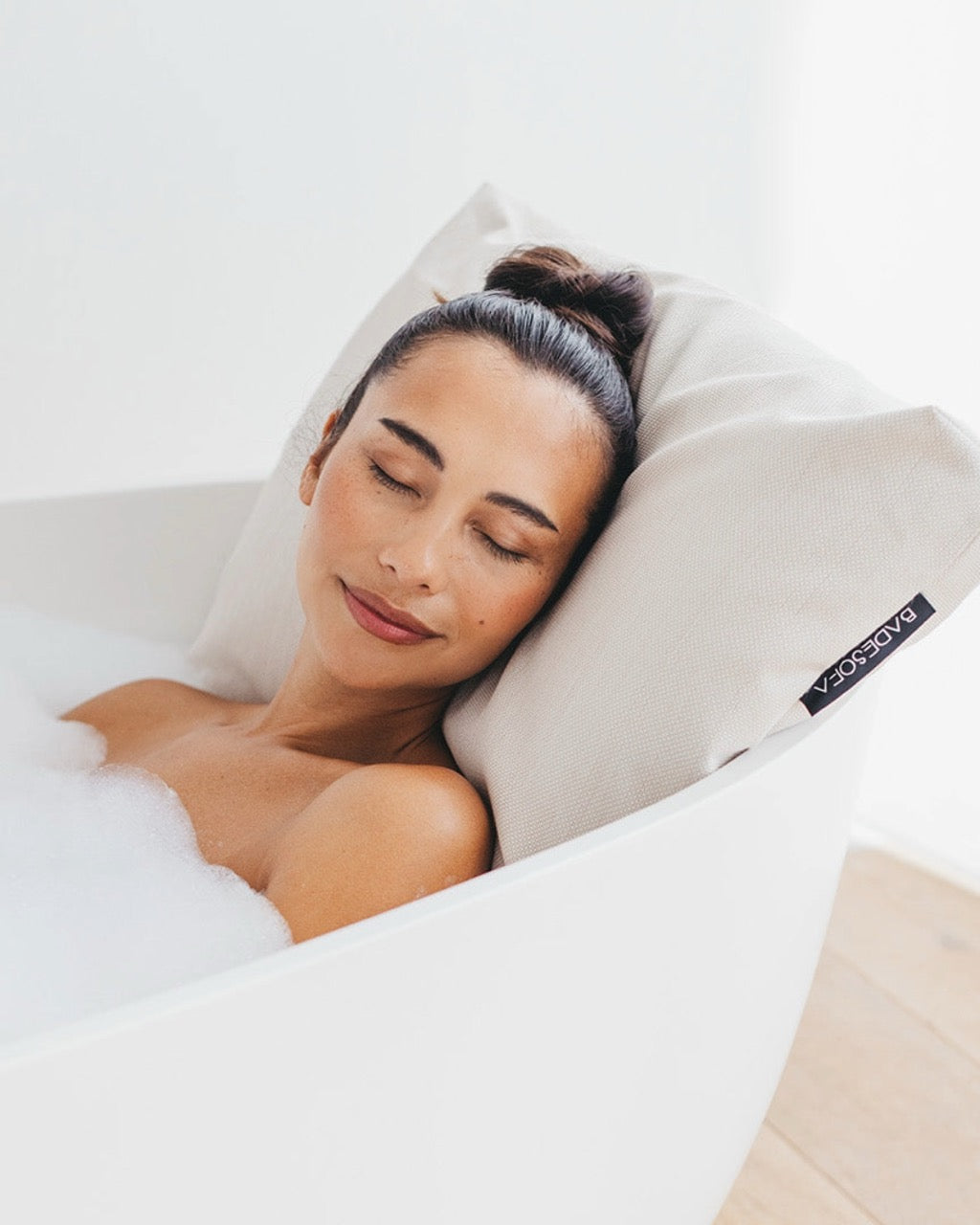 Perlmutt Badesofa Rückenkissen (Size Large) in einer freistehenden Badewanne, mit einer Frau, die sich entspannt anlehnt. $ Freistehende Badewanne | Size Large